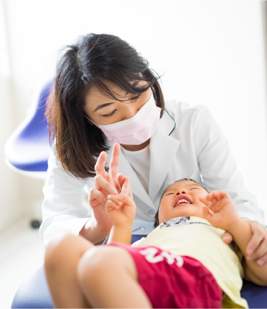 診療台でピースをするお子さまと笑顔で向き合う歯科医師