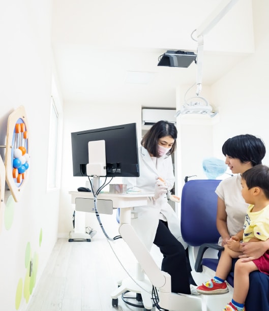 保護者のひざの上に座るお子さまに声をかけながら診療を進める歯科医師